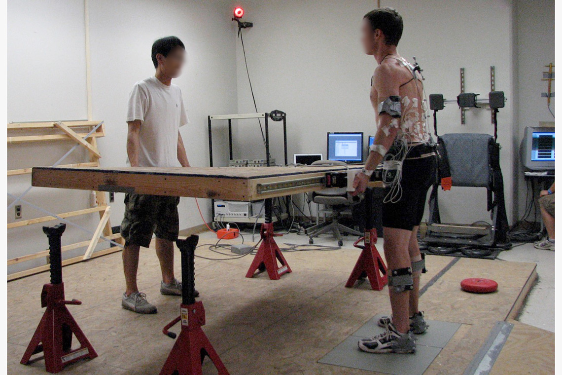 A participant (right) with sensors is moving a panelized wall with an experimenter (left) in the lab.